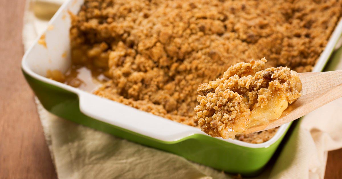 Scooping a serving of Apple Betty out of a baking dish with a wood spoon.
