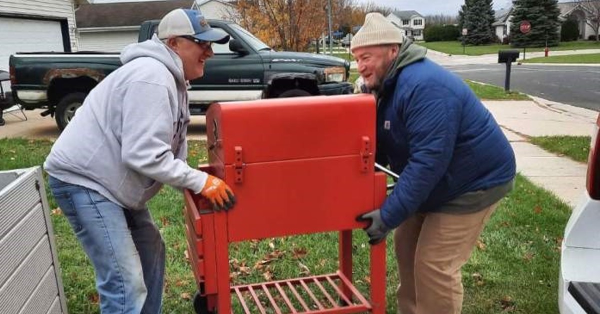 Lee Van De Hey, right, helps a friend lift a large red grill.