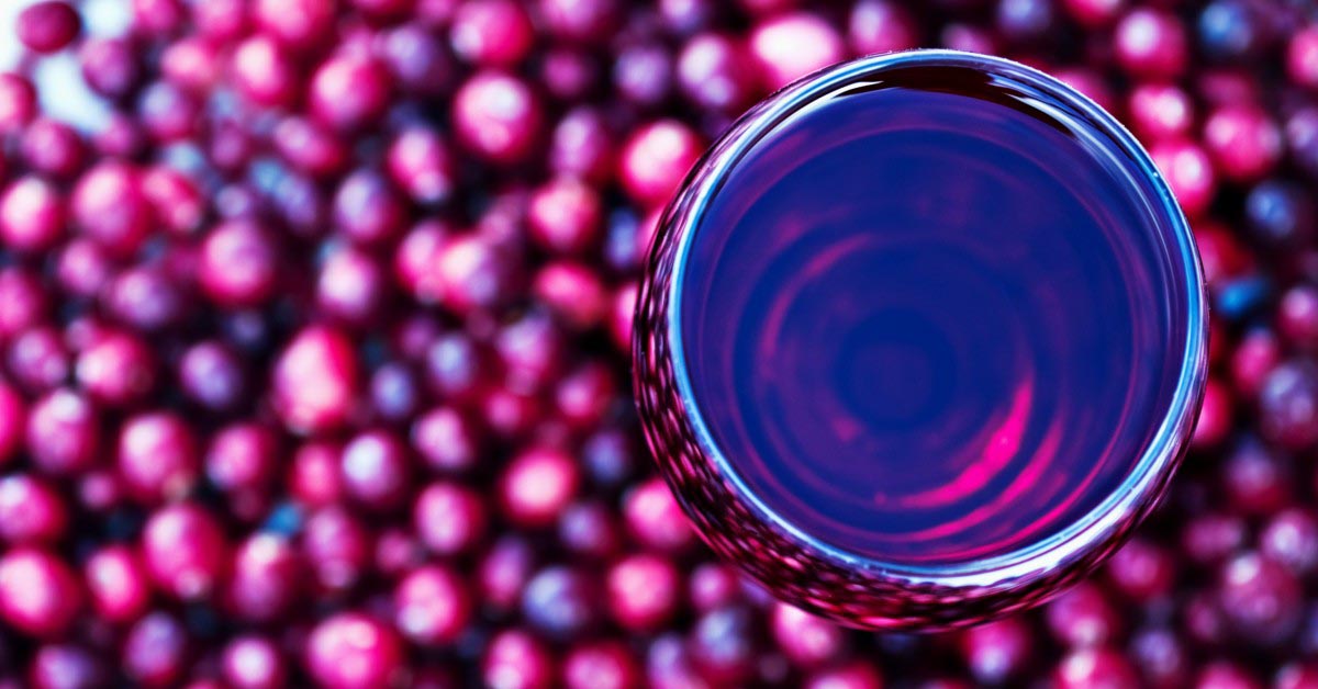 A glass of cranberry juice, surrounded by raw cranberries, seen from above.