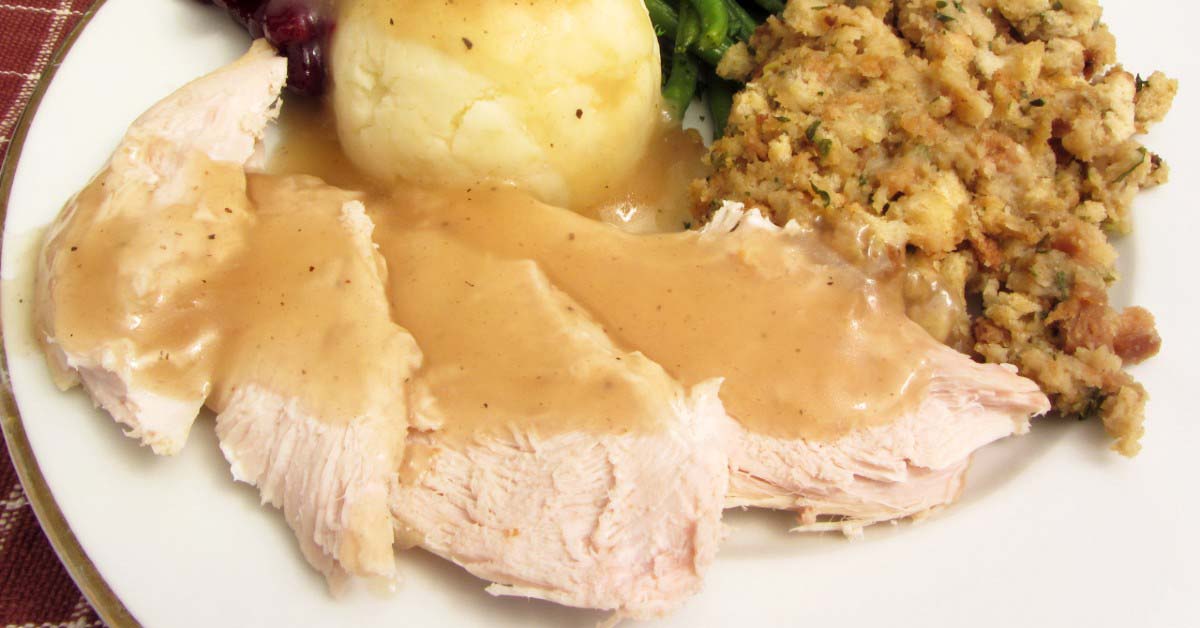 Sliced turkey, gravy, mashed potatoes and stuffing on a white plate.